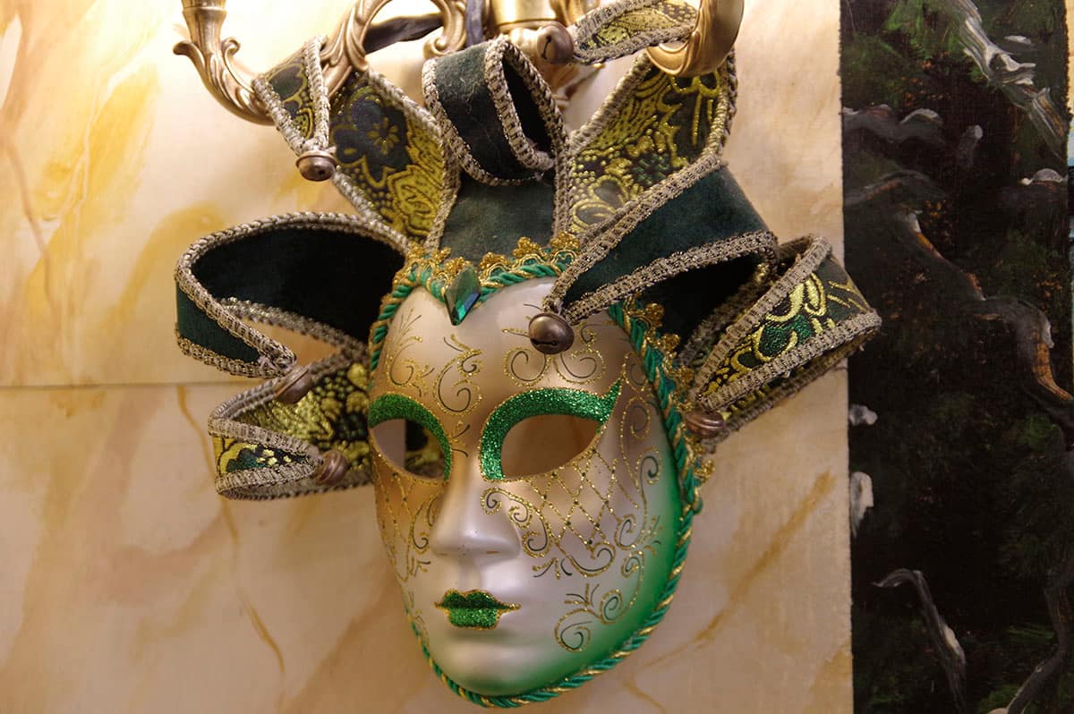 Masque vénitien vert et or accroché au mur de marbre peint de la salle.