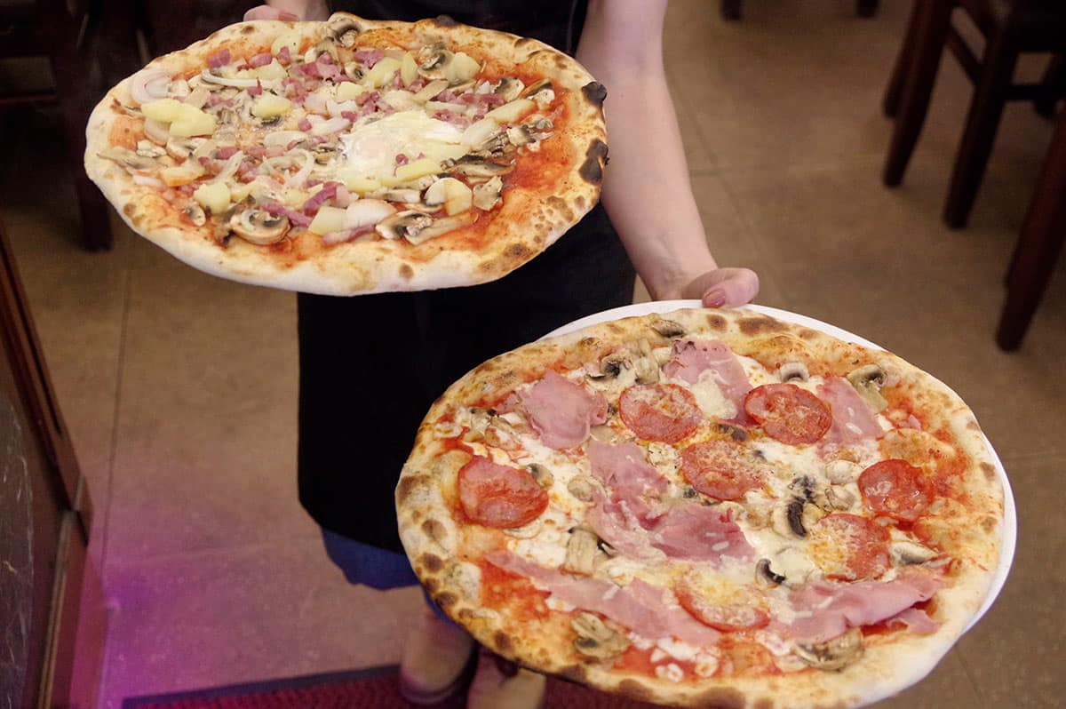 Deux pizzas à pâte fine portées en salle par un serveur.