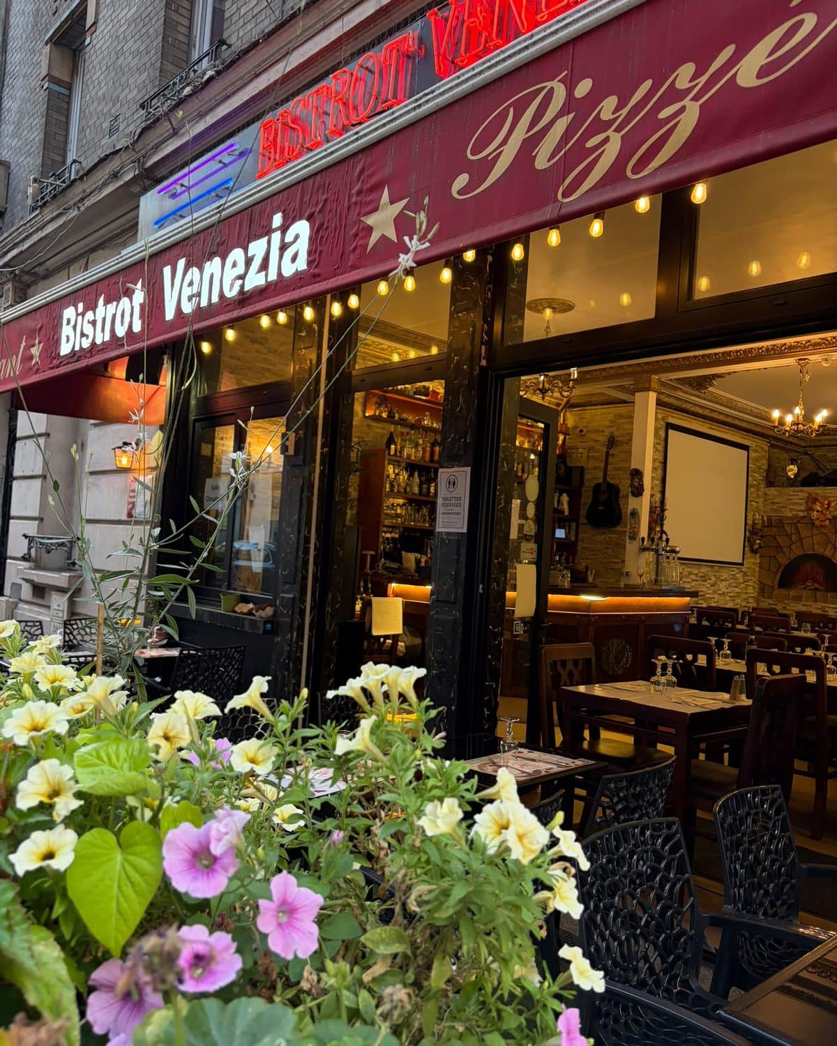 L’enseigne du Bistrot Venezia au-dessus des jardinières en fleurs, à la tombée du jour.