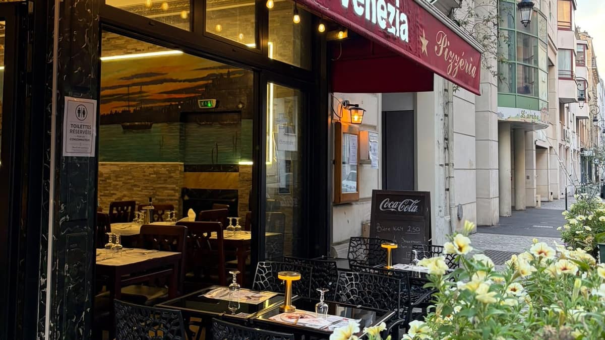 La devanture du Bistrot Venezia rue Godefroy : store rouge, terrasse et jardinières fleuries.