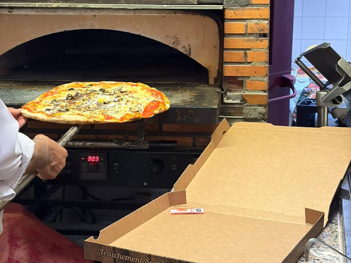Une pizza portée sur la pelle jusqu’à la bouche du four à bois en briques.