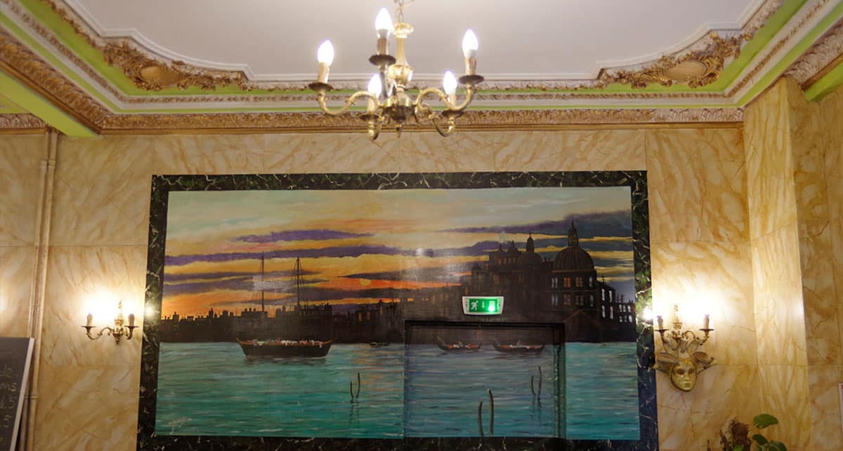 Peinture murale d’un coucher de soleil sur Venise, encadrée par la corniche ancienne de la salle.