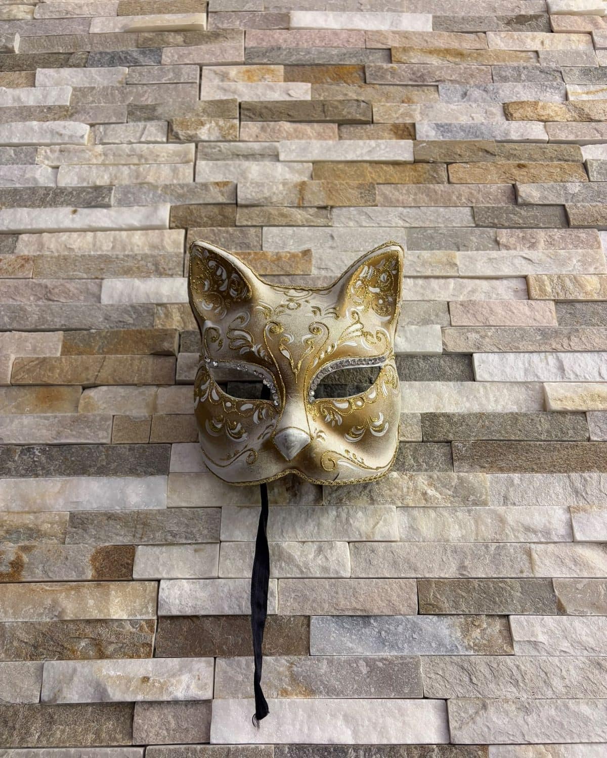Masque vénitien en forme de chat, doré et argenté, sur le mur de pierre claire.