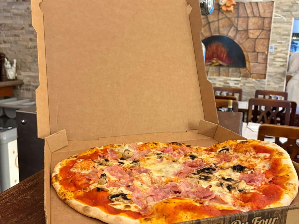 Pizza au jambon et aux champignons dans son carton, prête à emporter.