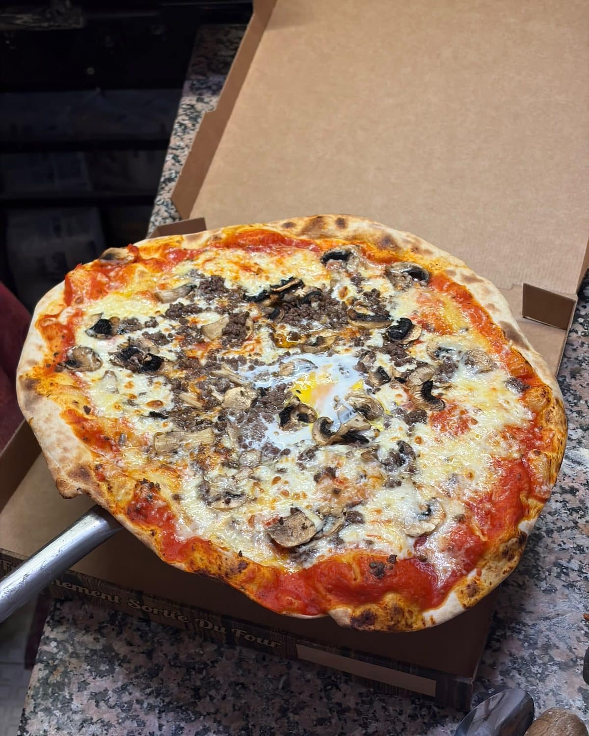 Pizza aux champignons et à l’œuf posée sur la pelle, au sortir du four.