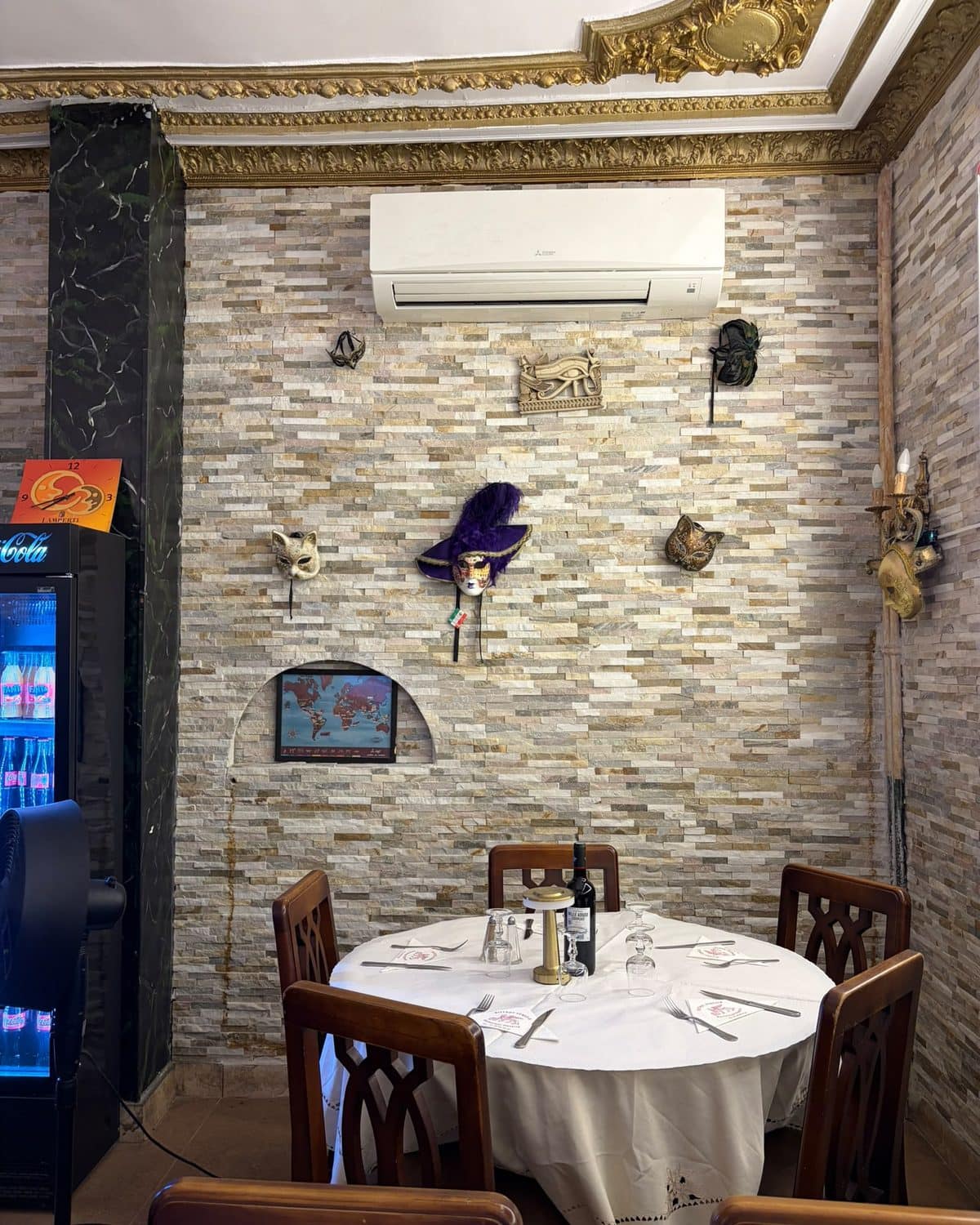 Coin de salle avec sa table ronde dressée, sous les masques vénitiens.