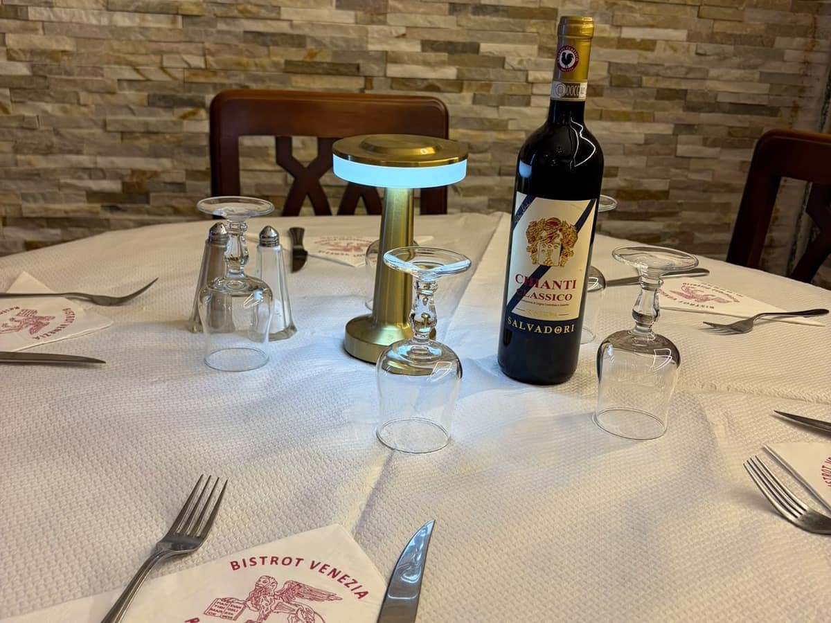 Table dressée : nappe blanche, serviette au logo de la maison, verres et couverts.