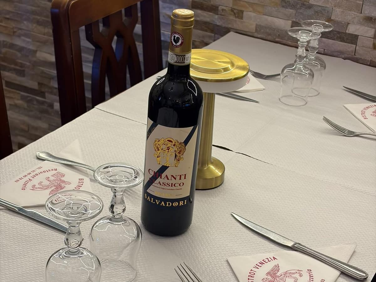 Table dressée avec une bouteille de chianti, verres retournés et serviettes au logo.